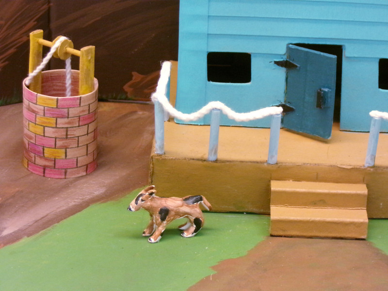 A detail photograph of the previous sculpture. This view shows the dog, well, porch, railing, and the front door of the house from close up.